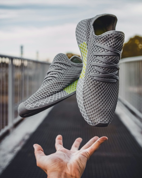 The original photo: grey mesh sneakers held above a hand on a bridge